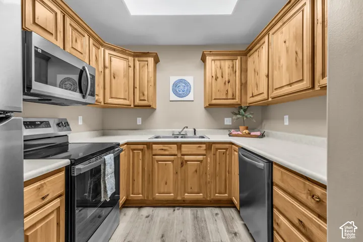 Kitchen featuring knotty wood cabinetry, light-toned countertops, stainless steel appliances, a double-basin sink, and a skylight