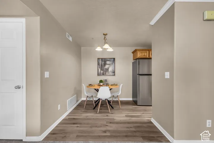 Dining area featuring wood-finish flooring, a multi-light chandelier, and a stainless steel refrigerator with built-in cabinetry above
