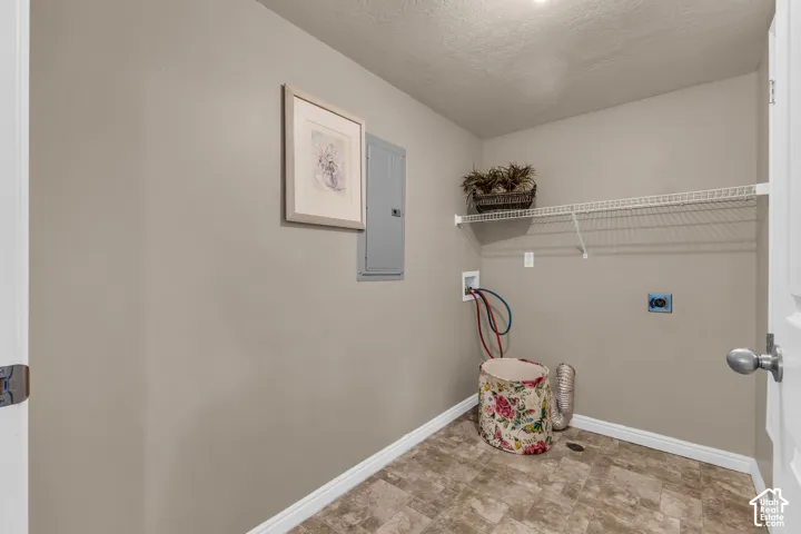 Laundry utility space featuring neutral-toned walls, tile-patterned flooring, a wall-mounted electrical panel, and built-in wire shelving