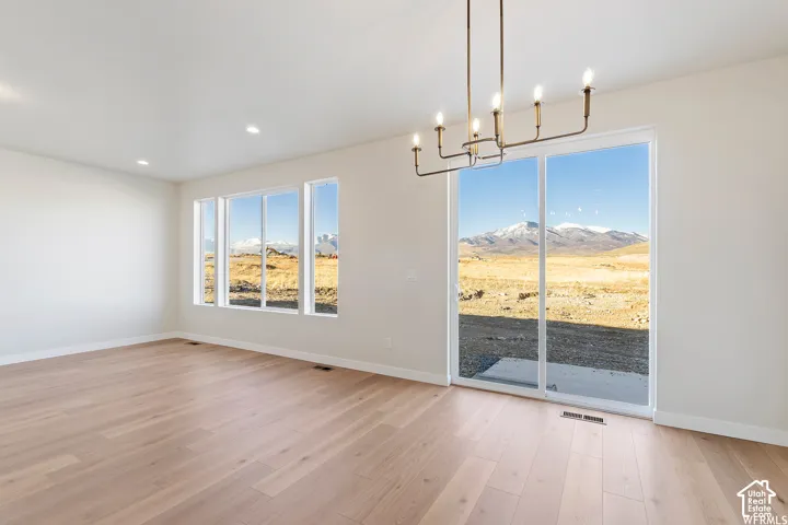 Open interior featuring light-tone wood-finish flooring, recessed lighting, a modern multi-arm chandelier, large-format windows, and sliding glass doors with mountain scenery