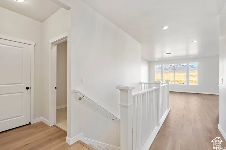 Interior landing featuring wood-finish flooring, white spindle railing, recessed lighting, and expansive windows with a mountain backdrop