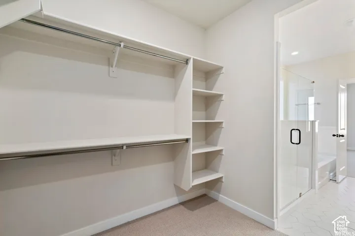 Walk-in closet with multi-tier hanging rods and built-in shelving, featuring carpeted flooring and an entry into a bathroom with a glass-enclosed shower