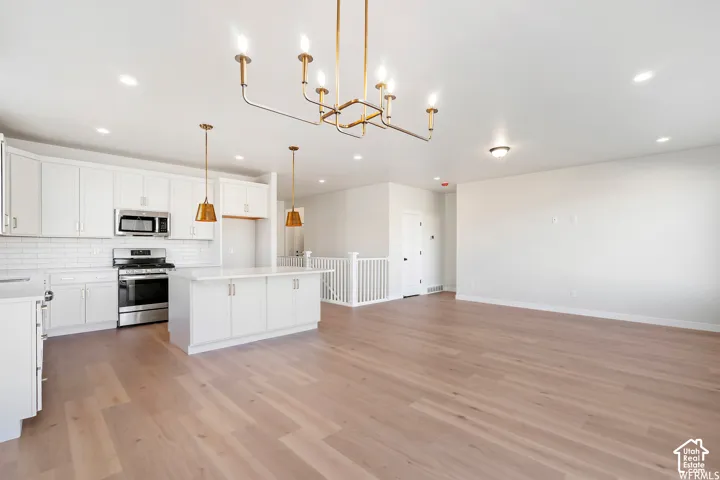 Open-concept space featuring wood-finish flooring, white cabinetry, an island with countertop seating, a subway tile backsplash, and a multi-arm metallic chandelier