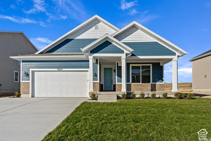 Exterior featuring blue horizontal siding, decorative shake accents, brick masonry wainscoting, a covered front porch with square columns, and an attached two-car garage