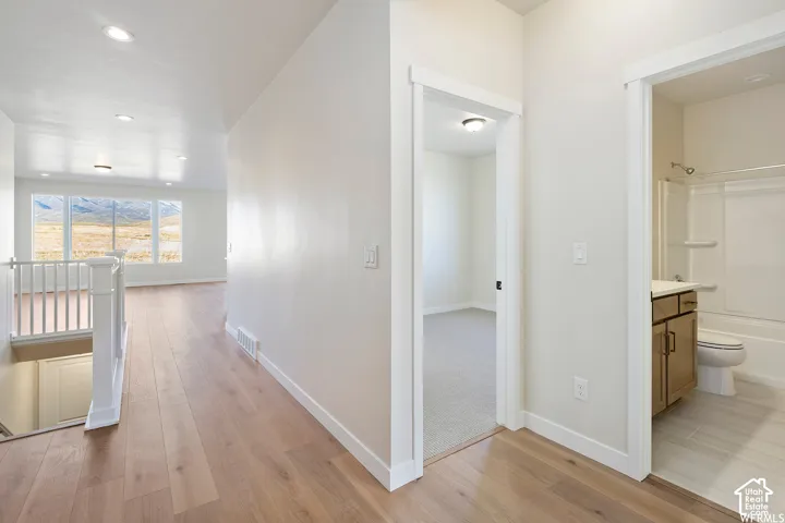 Hallway featuring wood-finish flooring, recessed lighting, white stair railing, and neutral wall-to-wall carpeting in the bedroom