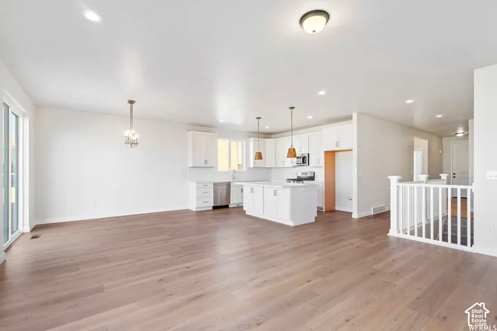 Open-concept kitchen featuring white shaker-style cabinetry, a central island with countertop seating, wood-finish flooring, recessed lighting, and sliding glass door access