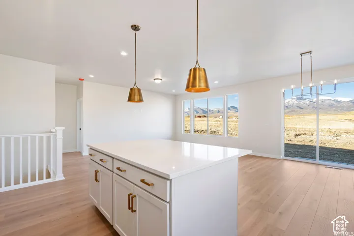 Kitchen island with stone countertop, wood-finish flooring, brass-tone pendant lighting, large sliding glass door, and mountain backdrop