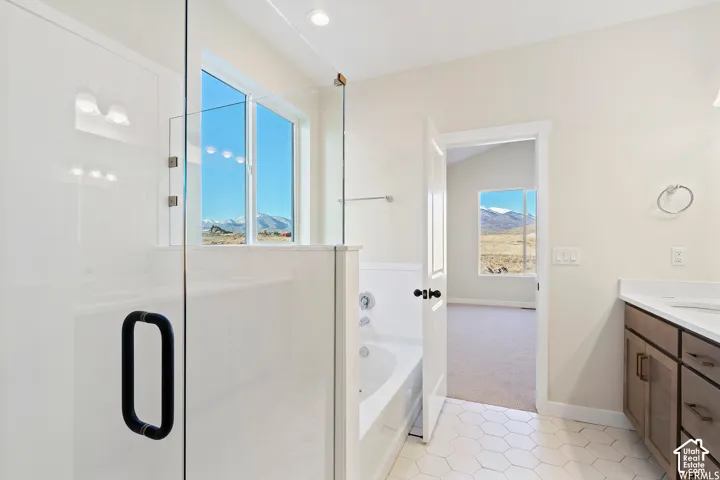 Bathroom featuring a glass-enclosed shower, deep soaking tub, white hexagon tile flooring, vanity with neutral-toned cabinetry, and mountain scenery