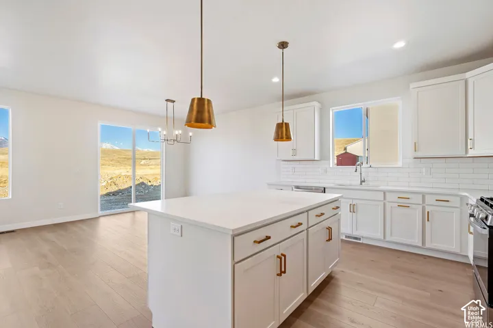Kitchen featuring white cabinetry, an oversized central island with a solid surface countertop, wood-finish flooring, subway tile backsplash, and metallic pendant lighting