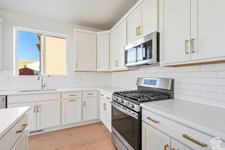Kitchen featuring white shaker-style cabinetry with gold-tone pulls, quartz countertops, white subway tile backsplash, and stainless steel appliances including a gas range