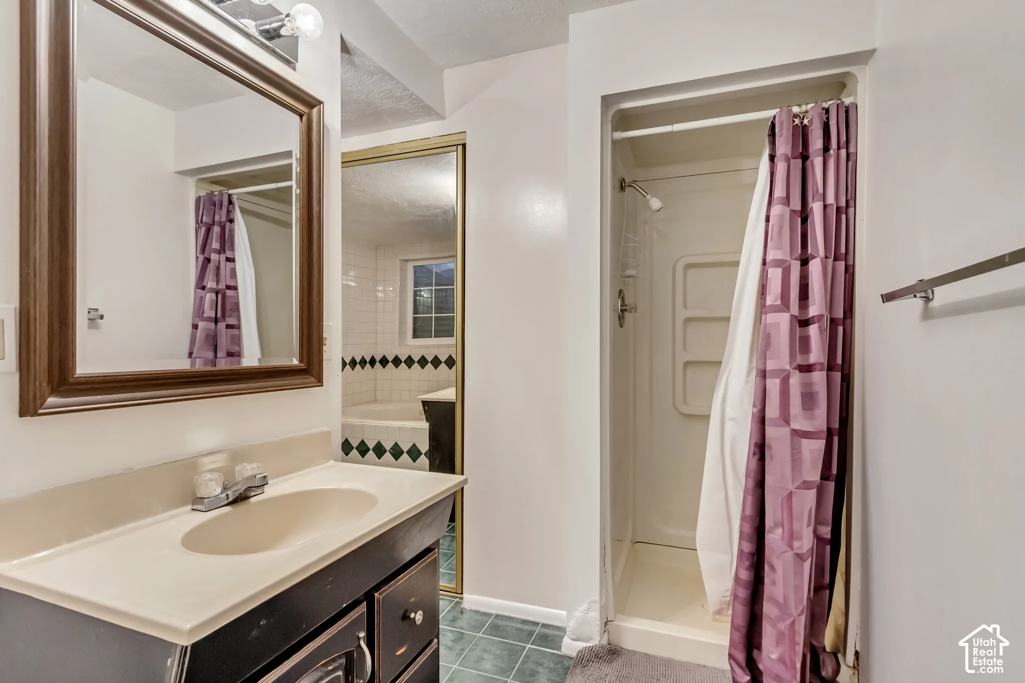 Bathroom featuring a vanity with an integrated countertop, wall-mounted mirror, stand-up shower stall with built-in shelving, and tile flooring