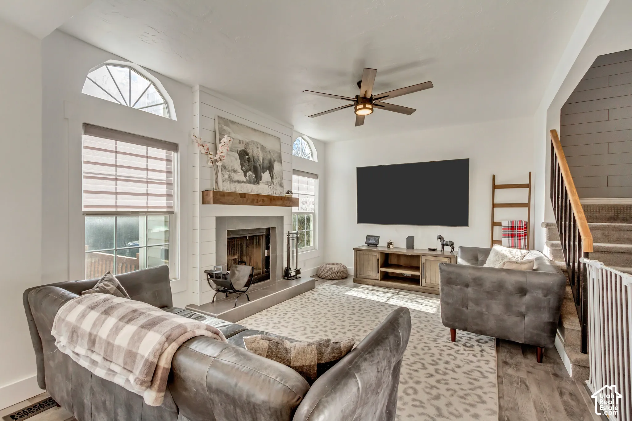 Living area featuring a fireplace with a horizontal shiplap surround, natural wood mantel, arched transom windows, and a ceiling fan