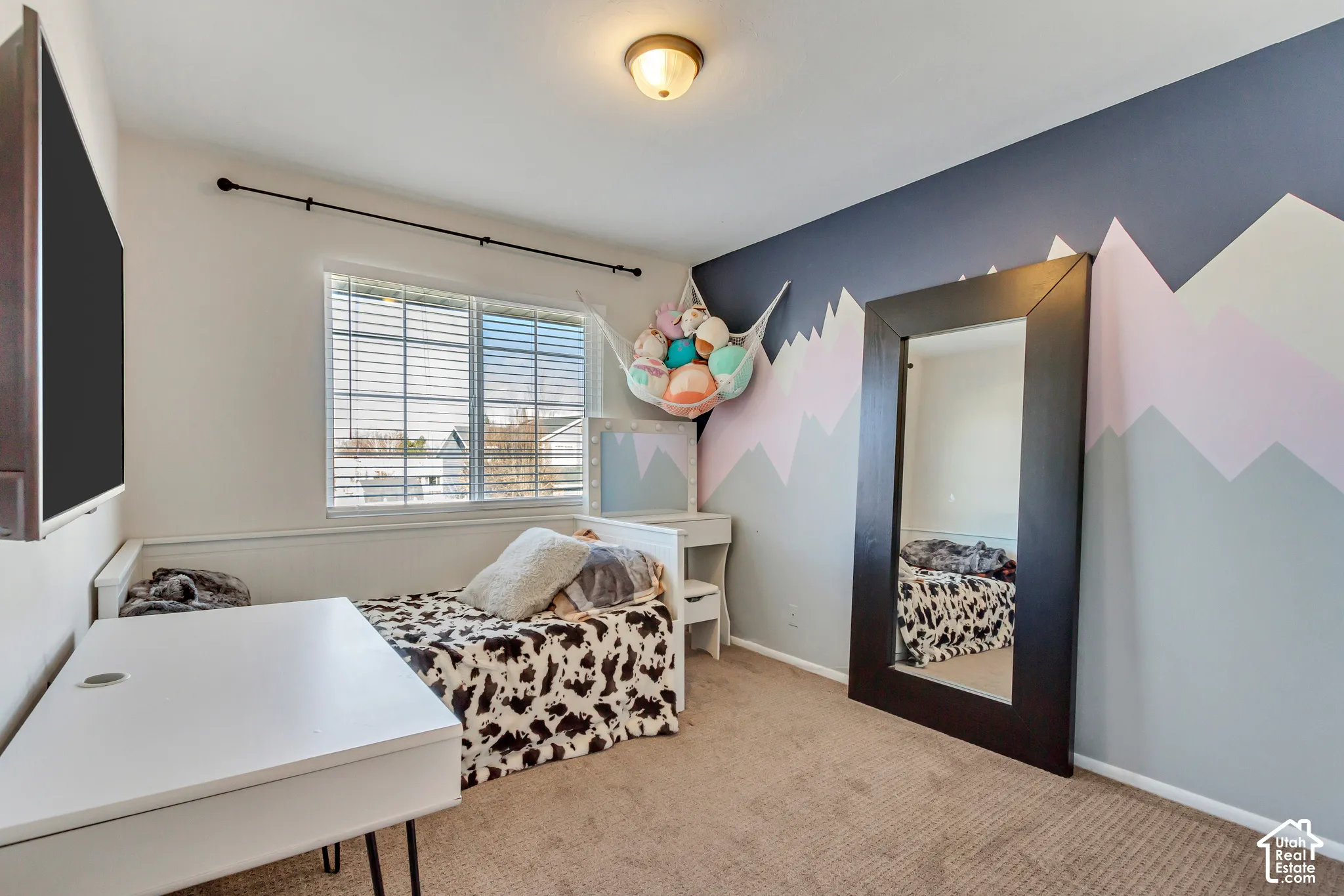 Bedroom featuring neutral carpeting, a dual-pane window with horizontal blinds, a decorative wall mural, and a central flush-mount ceiling light fixture