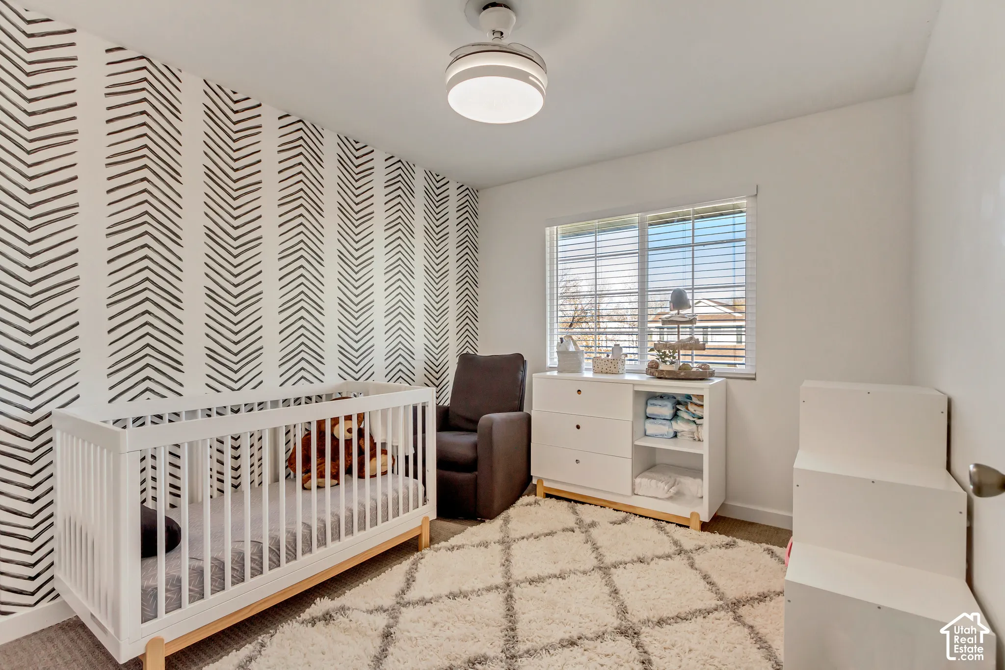 Room featuring a patterned accent wall, neutral carpeting, horizontal window blinds, and a modern integrated ceiling fan with a light fixture