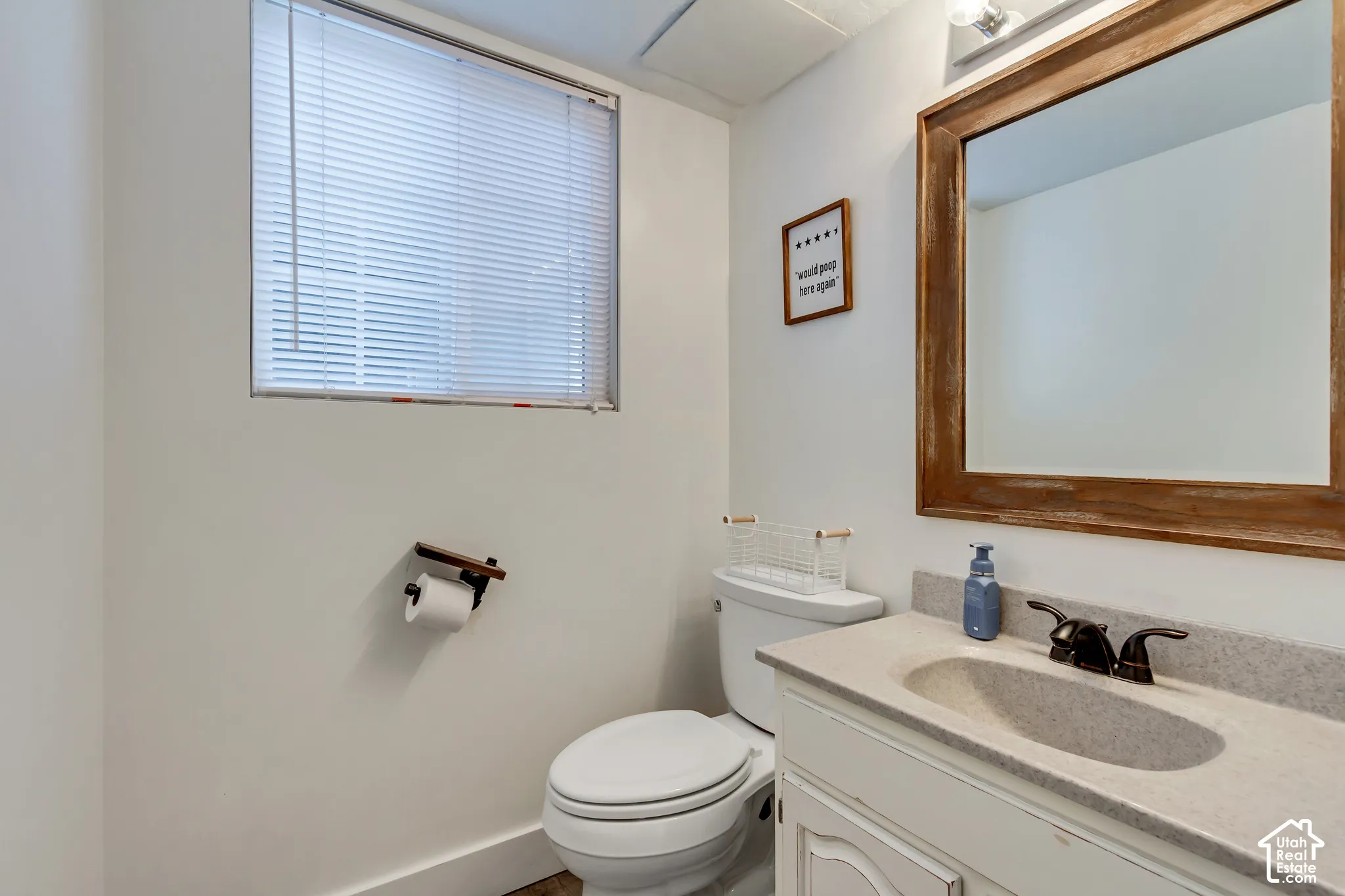 Bathroom featuring a vanity with an integrated basin, stone-composite countertop, and oil-rubbed bronze faucet, paired with a wood-framed mirror and horizontal blind window treatment