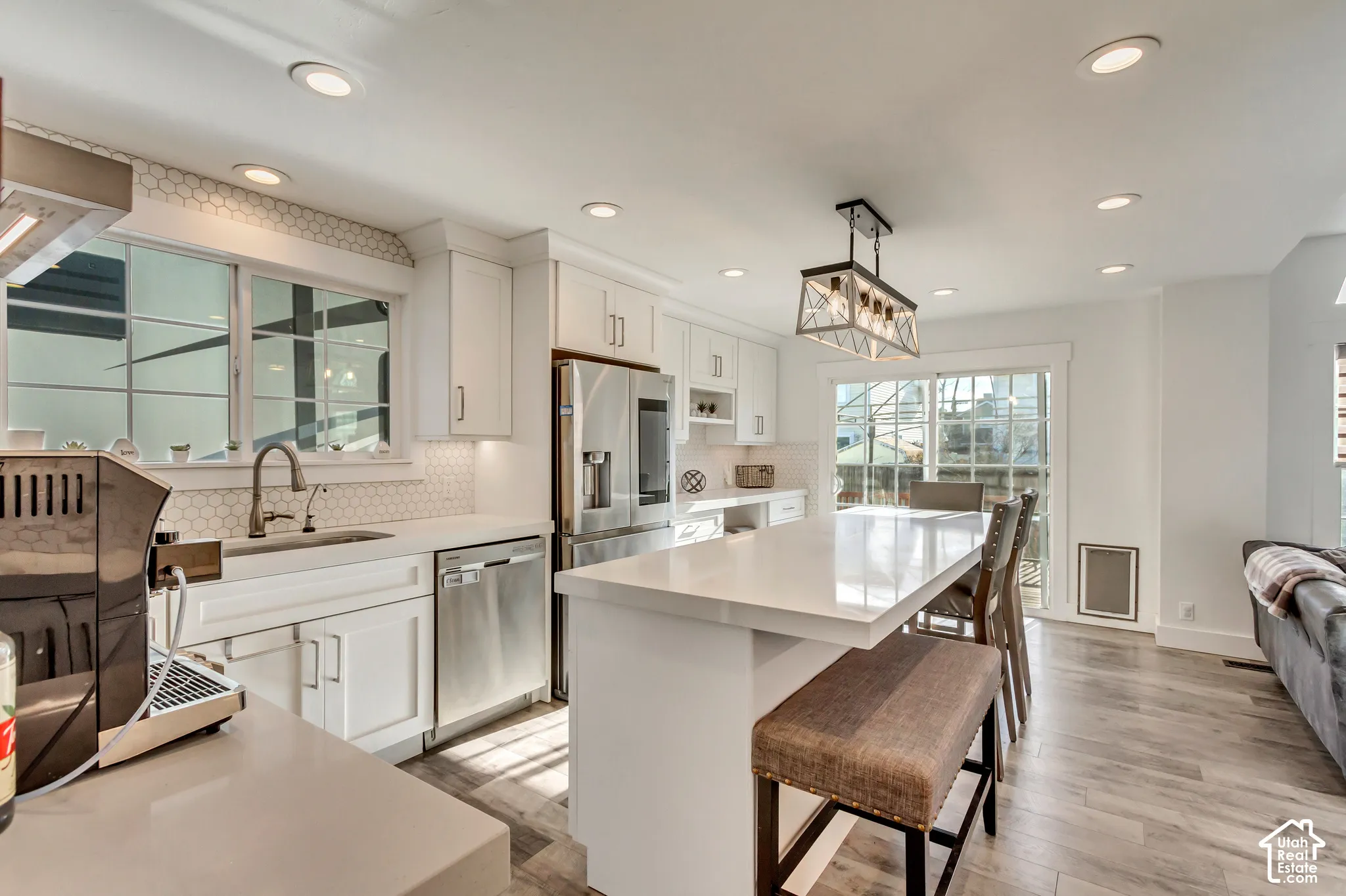 Kitchen featuring a center island with a solid surface countertop, white cabinetry, hexagon tile backsplash, stainless steel appliances, and wood-finish flooring