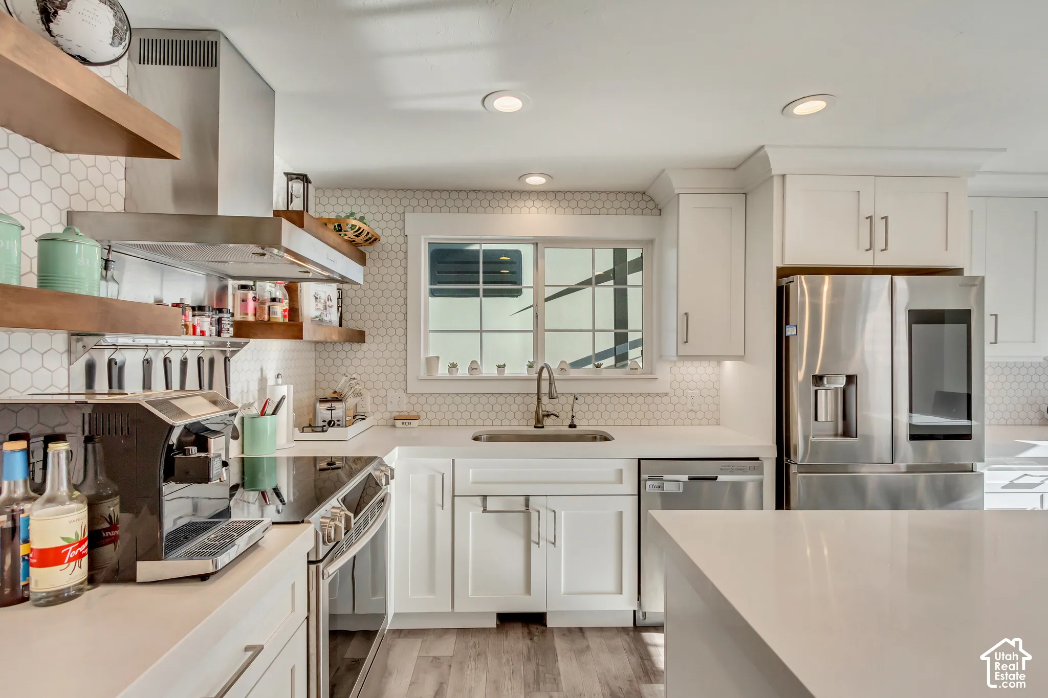 Kitchen featuring white cabinetry, quartz countertops, white hexagonal backsplash tile, stainless steel appliances, and wood-finish flooring