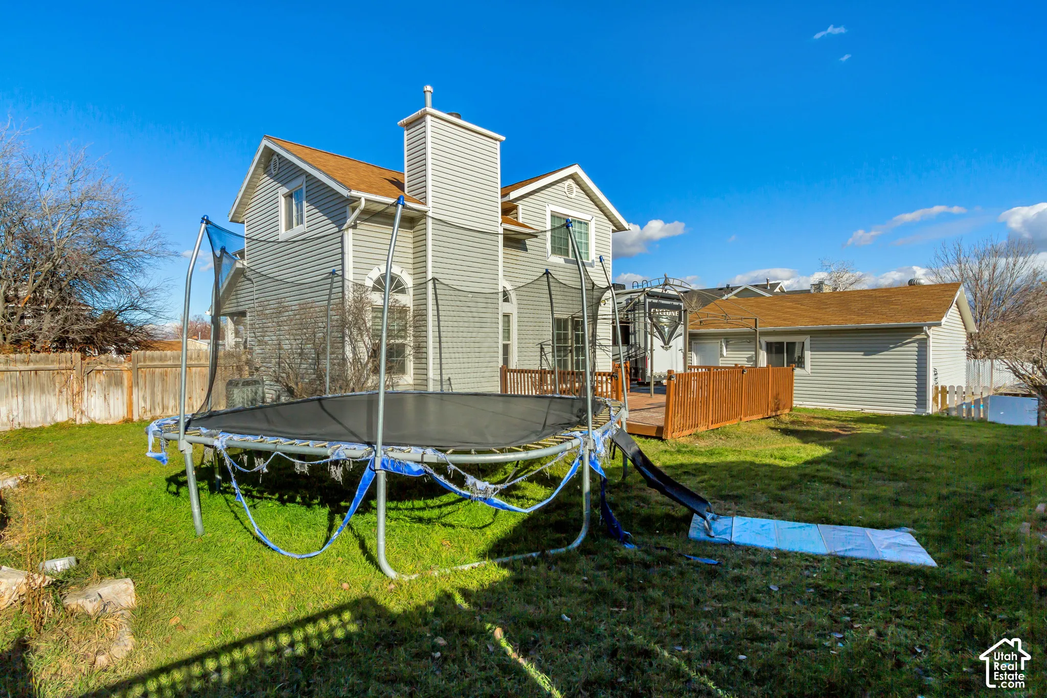 Exterior featuring vinyl siding, shingled roofing, a prominent chimney, a wood deck, and wood-panel perimeter fencing