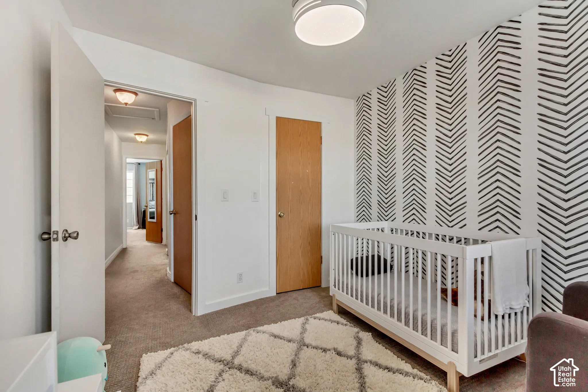 Room featuring a bold geometric accent wall, neutral carpeting, and a flush-mount ceiling light fixture
