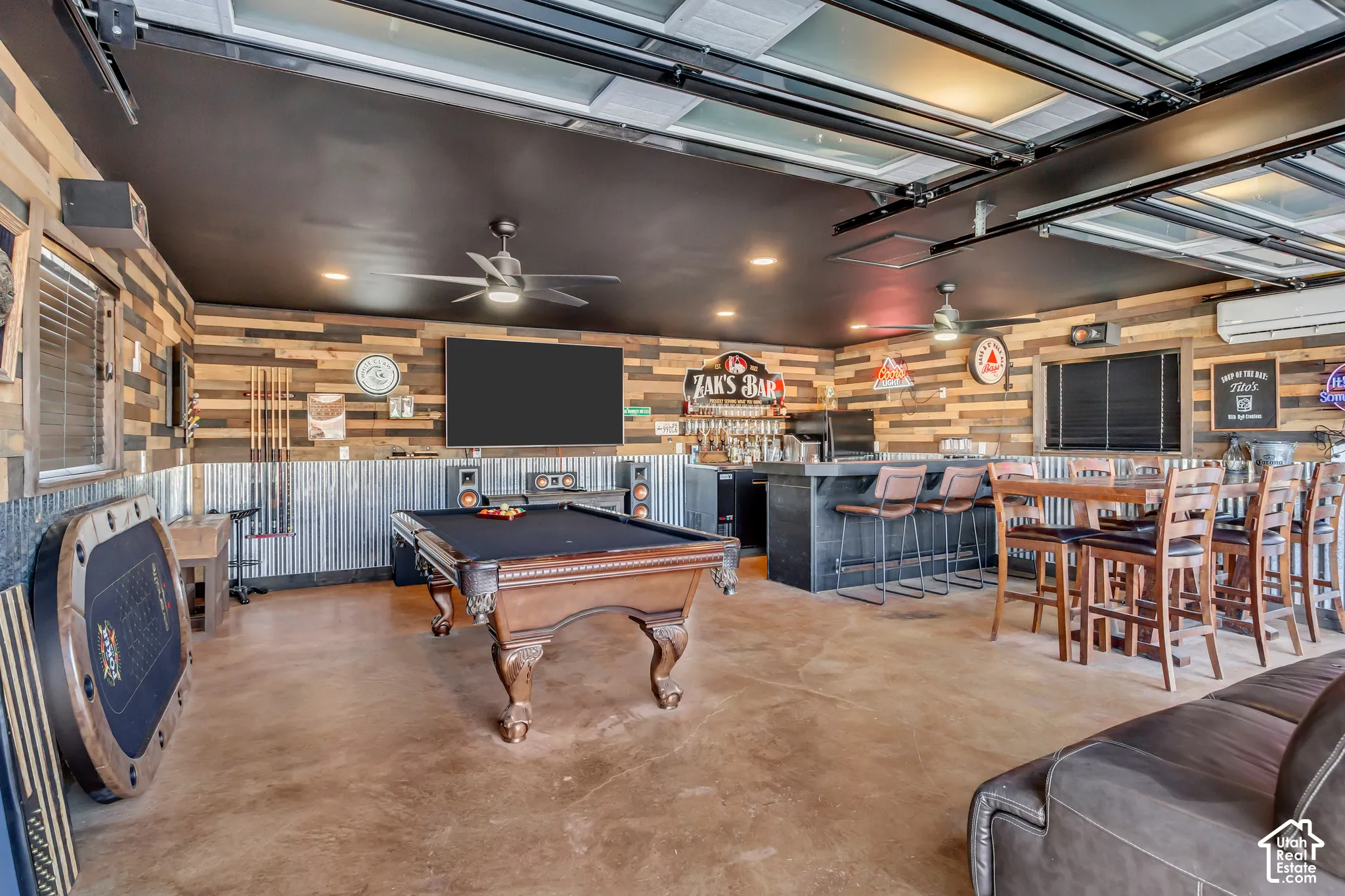 Multi-purpose flex space featuring industrial-style corrugated metal and wood-plank wall treatments, concrete flooring, overhead glass-paneled garage door, and recessed lighting