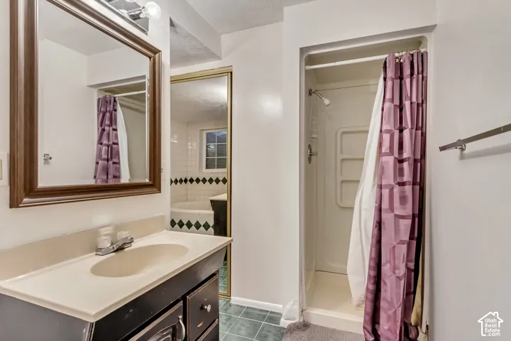 Bathroom featuring a vanity with an integrated countertop, wall-mounted mirror, stand-up shower stall with built-in shelving, and tile flooring