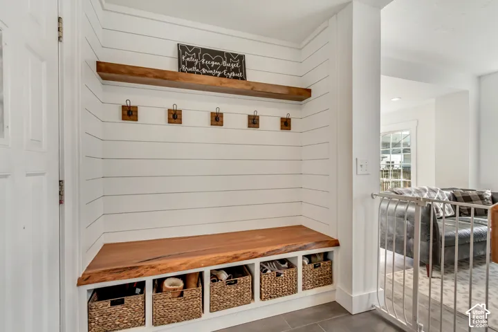 Built-in mudroom bench with a natural edge wood seat, white shiplap wall paneling, five mounted metal coat hooks, and a matching floating wood shelf above