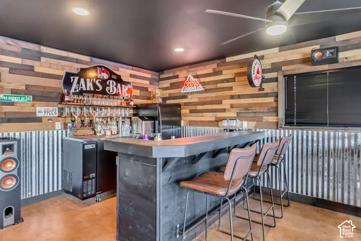 Wet bar featuring a dark-stained wood-finish counter, corrugated metal wainscoting, multi-toned wood-finish wall paneling, and a ceiling-mounted fan