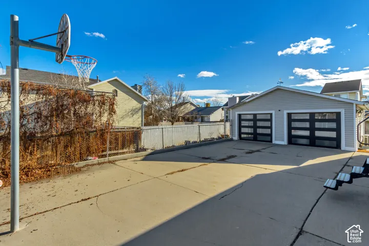 Detached two-car garage featuring modern paneled doors with horizontal glass inlays, concrete parking pad, and attached basketball hoop