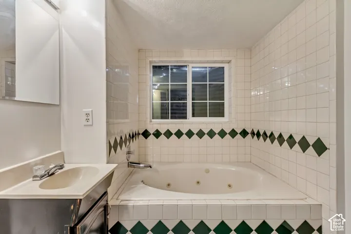 Built-in jetted soaking tub featuring white tile surround with green diamond accent inlay, integrated basin vanity, and grid-pattern window