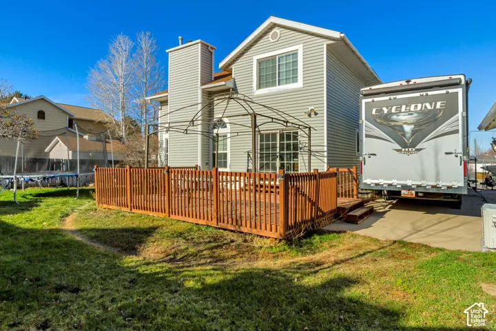 Exterior view featuring light grey vinyl siding, an elevated wood deck, a metal gazebo frame, and a concrete patio slab