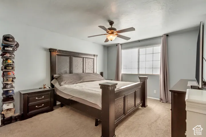 Carpeted bedroom featuring a grid-pattern window, ceiling fan with integrated lighting, and neutral wall color