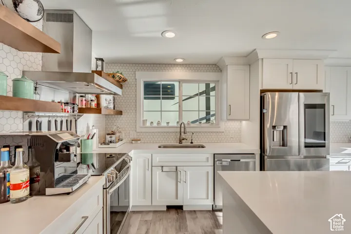 Kitchen featuring white cabinetry, quartz countertops, white hexagonal backsplash tile, stainless steel appliances, and wood-finish flooring