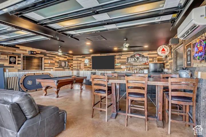 Garage space featuring a retractable glass-panel door, wood-plank wall treatments, corrugated metal wainscoting, polished concrete flooring, and a wall-mounted ductless climate control system