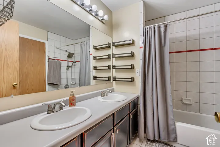 Dual-basin vanity with solid-surface countertop, full-width vanity mirror, built-in wall shelving, shower and tub combination with tile surround, and metallic finish hardware