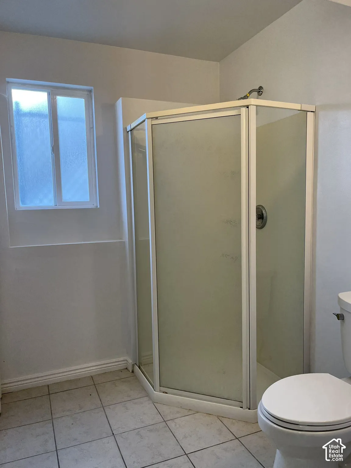 Corner shower enclosure with frosted glass panels, neutral ceramic tile flooring, and a sliding window