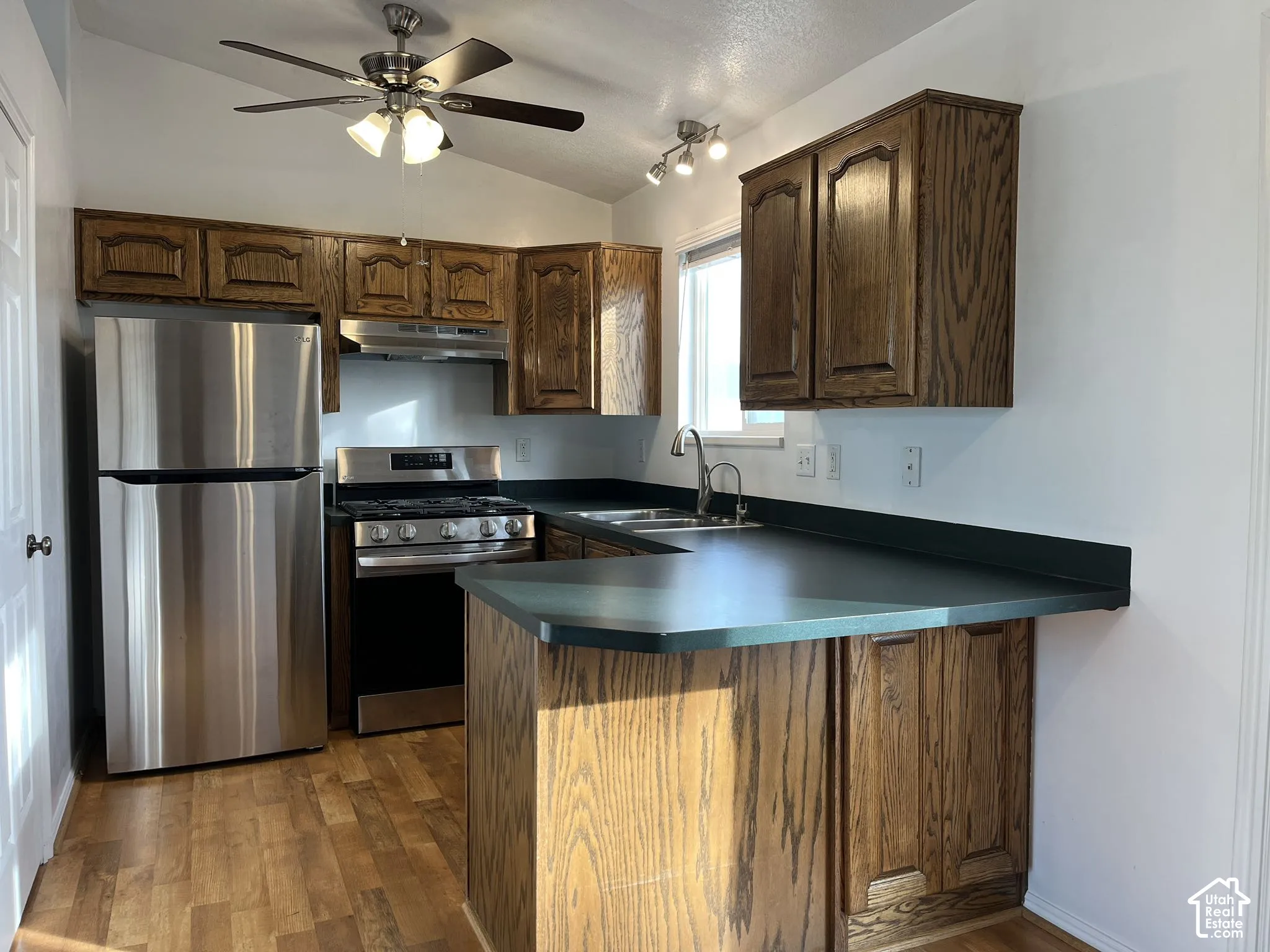 Kitchen featuring stained wood cabinetry, stainless steel appliances, solid surface countertops, wood-finish flooring, and a ceiling fan