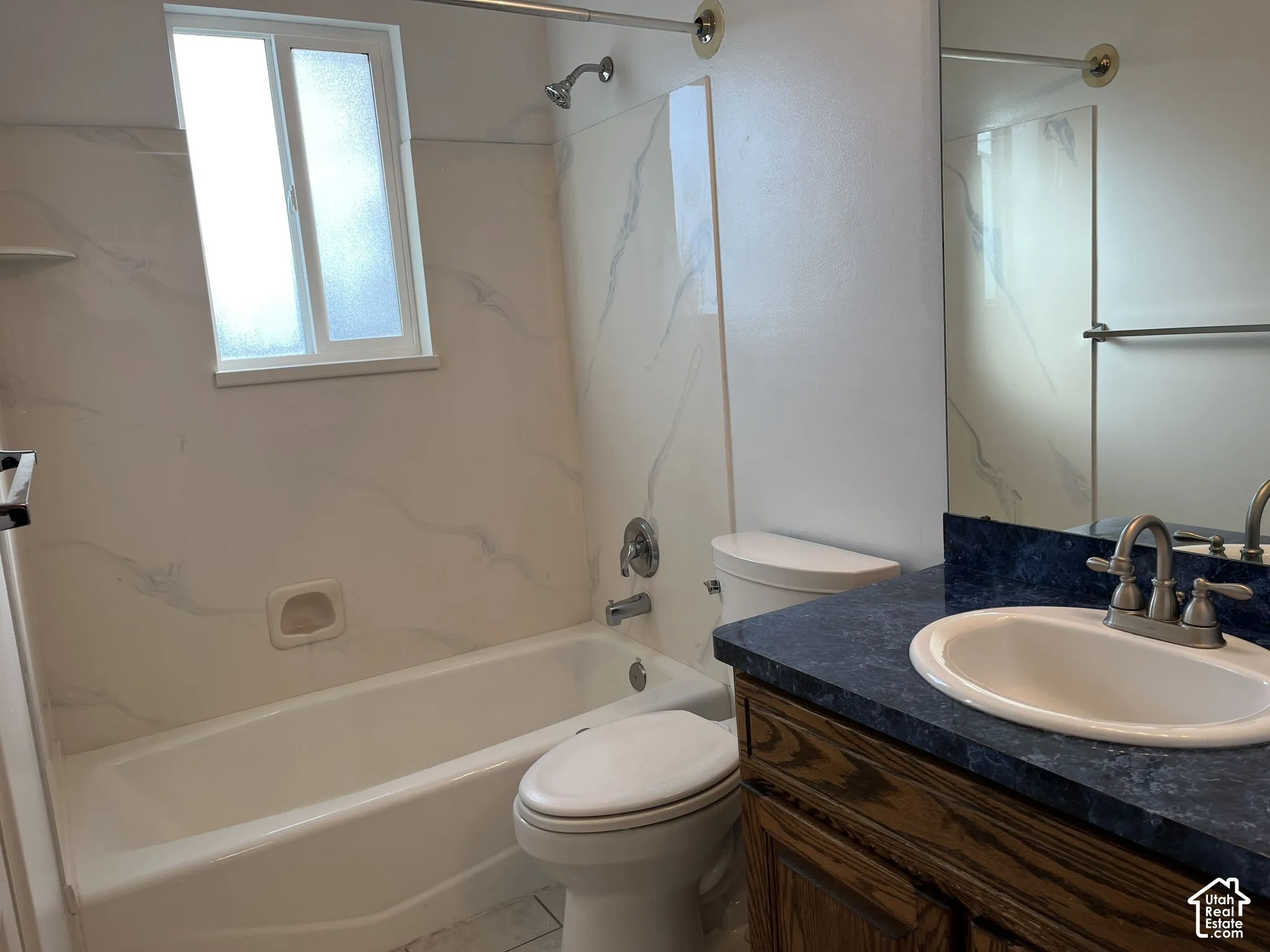 Bathroom featuring a vanity with a dark-toned countertop, integrated white sink, shower-tub combination with wall surround, and a wall-mounted mirror