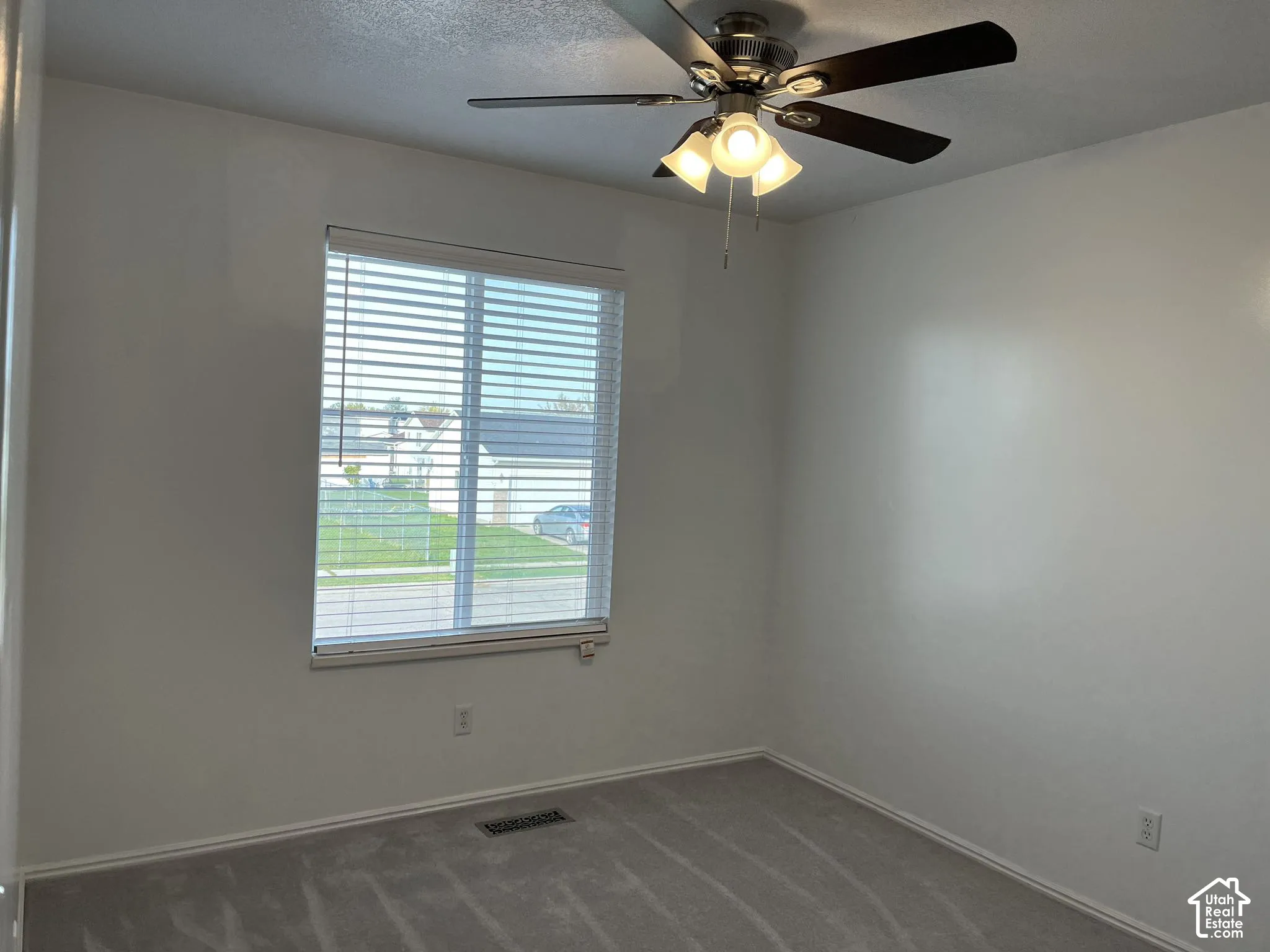 Room featuring neutral-toned carpeting, a window with horizontal blinds, and a multi-blade ceiling fan with integrated glass light fixtures