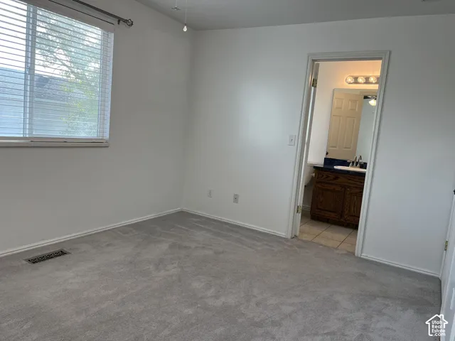 Neutral-toned carpeting, horizontal window blinds, and interior entry with wooden vanity cabinetry featuring a countertop with an integrated basin