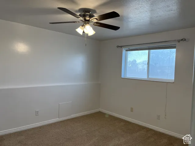 Neutral-toned wall-to-wall carpeting, ceiling fan with integrated three-light fixture, and sliding window with metal curtain rod