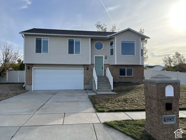 Bi-level exterior featuring horizontal siding, brick masonry, an attached two-car garage, concrete driveway, and an octagonal accent window