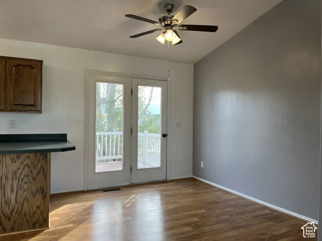Wood-finish flooring, vaulted ceilings, double glass doors with direct exterior access, and a multi-blade ceiling fan with integrated lighting