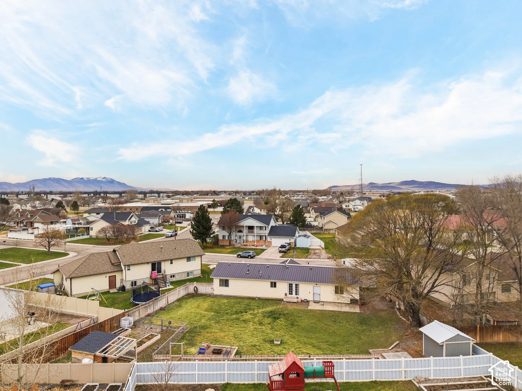 Expansive backyard featuring a white vinyl privacy fence, mature trees, a storage shed, and a mountain range backdrop