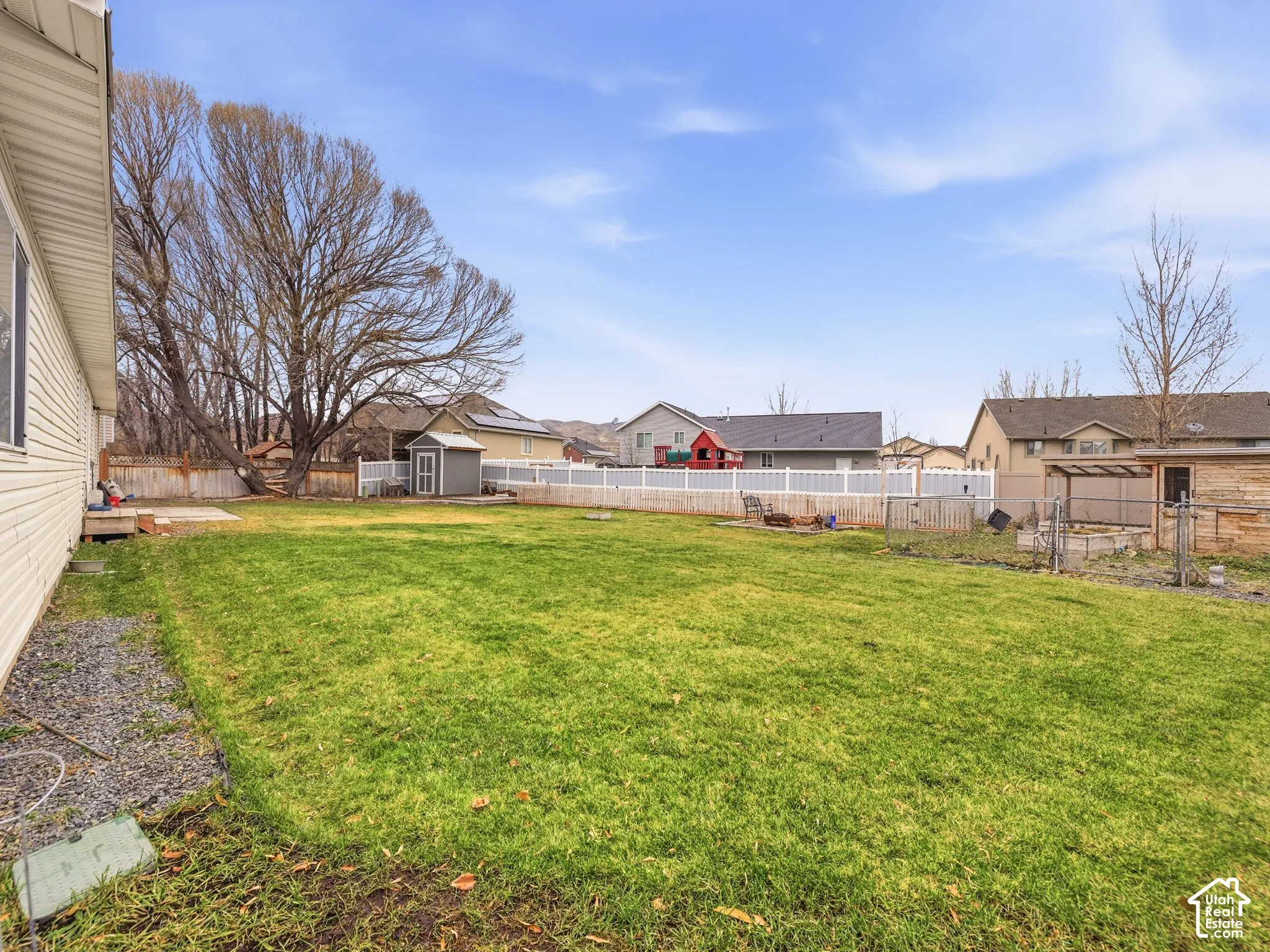 Expansive backyard featuring a large grass lawn, white vinyl fencing, a detached storage shed, and a fenced enclosure