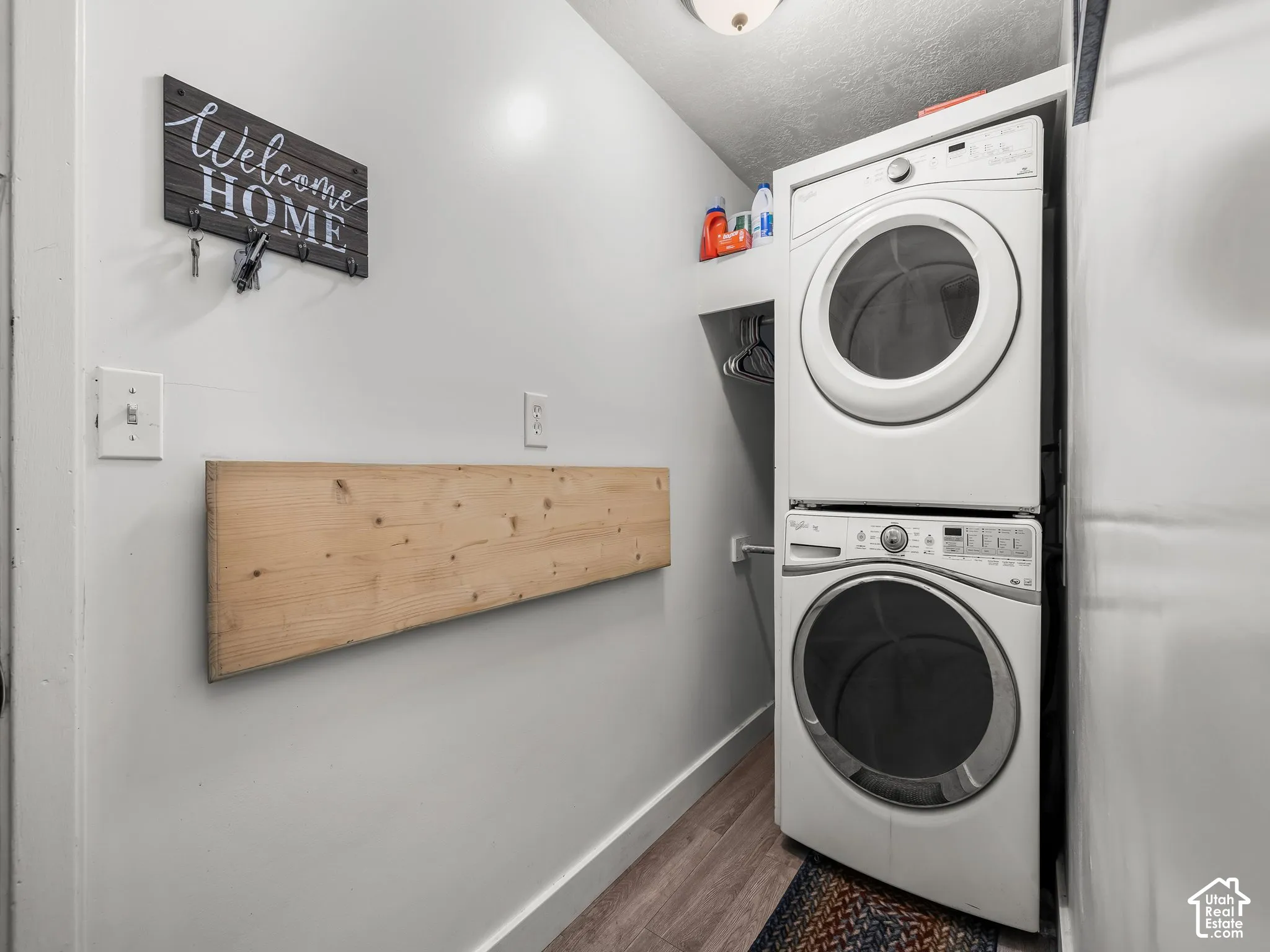 Laundry area featuring stacked laundry appliances, integrated shelving, wood-finish flooring, and a wall-mounted wood shelf