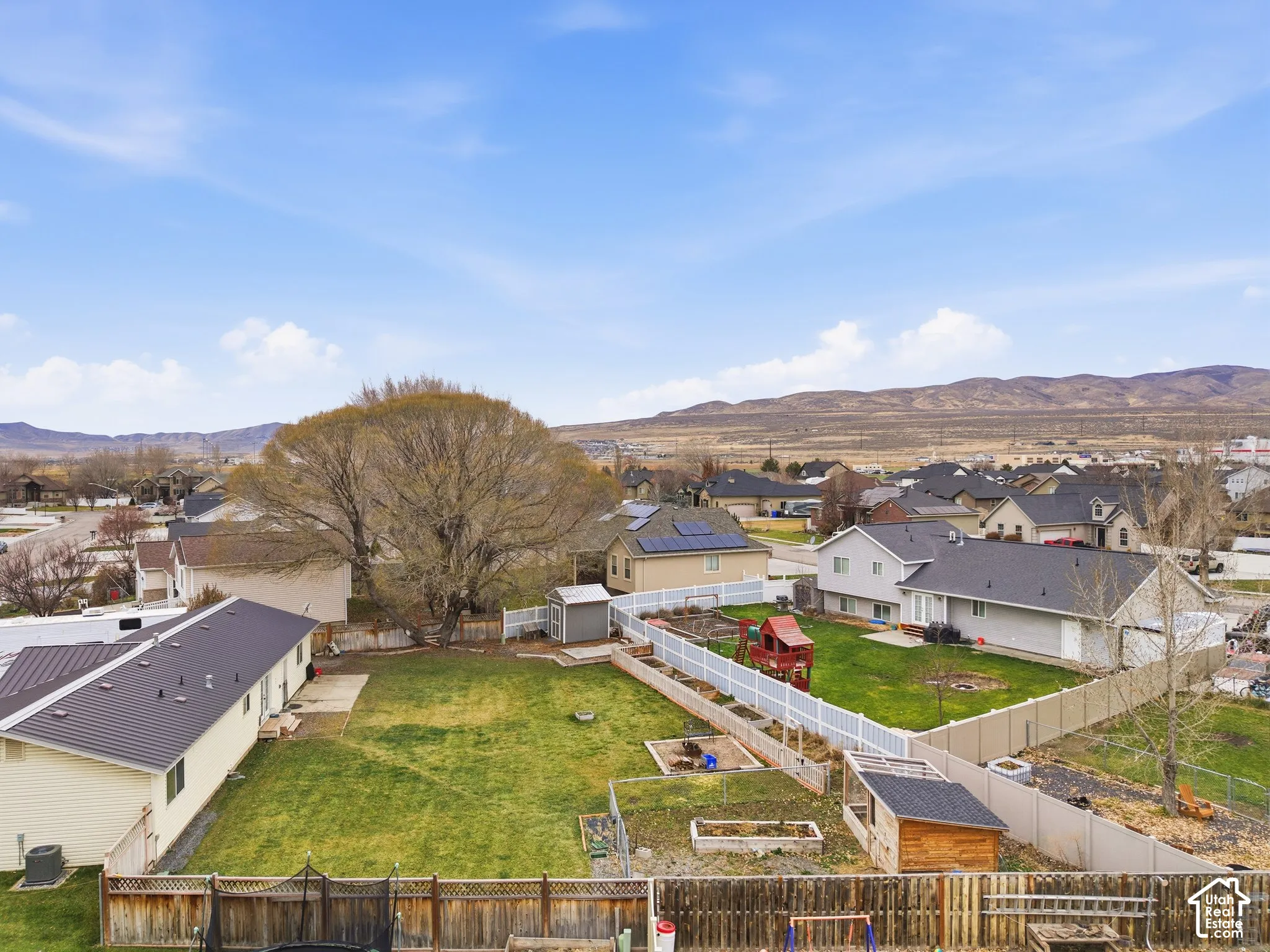 Expansive backyard featuring a fenced perimeter, raised garden beds, mature trees, and a storage structure, set against a mountain backdrop