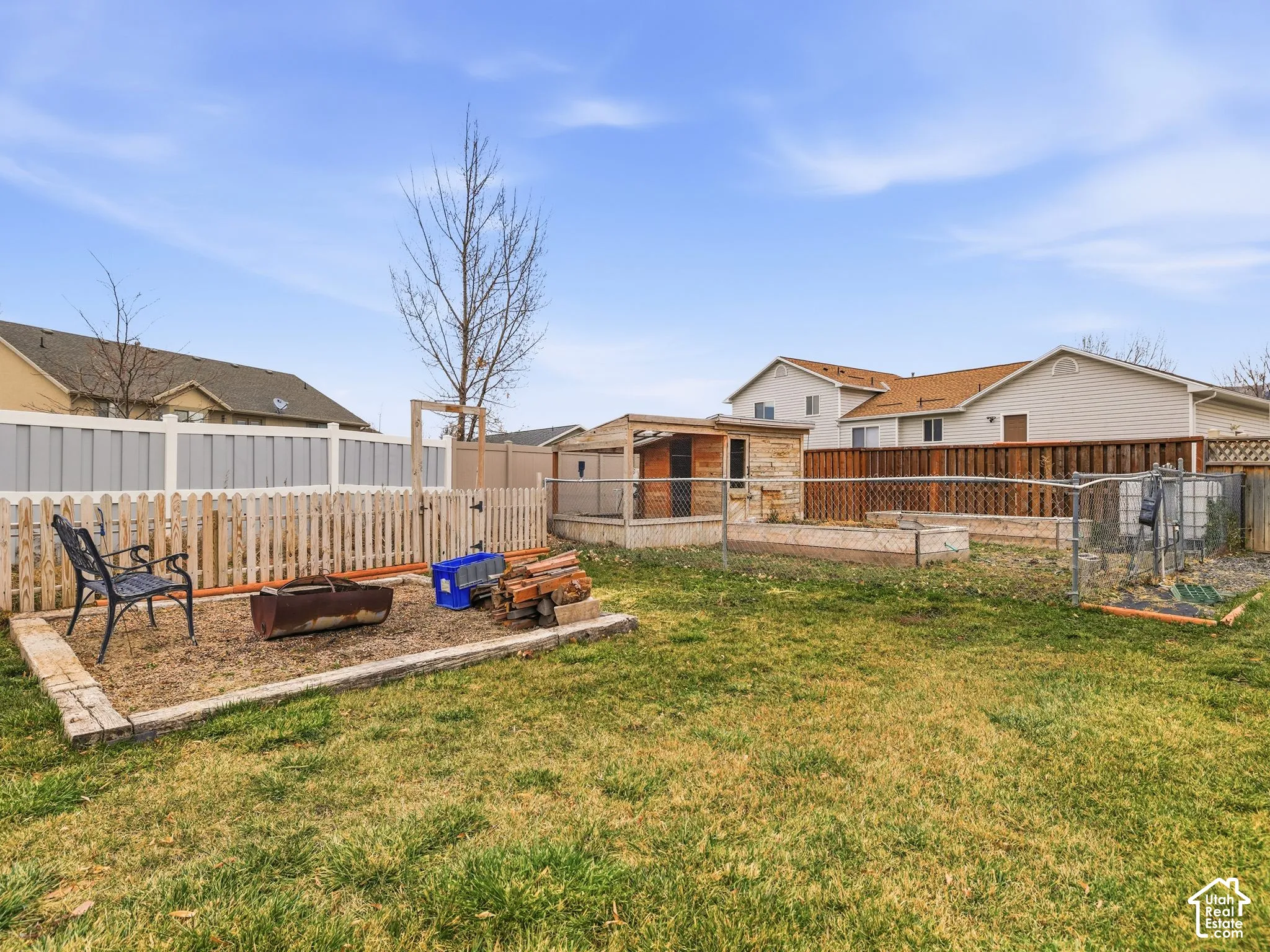 Rear yard featuring wood-border landscaping, a combination of picket and chain-link fencing, and a detached wooden structure