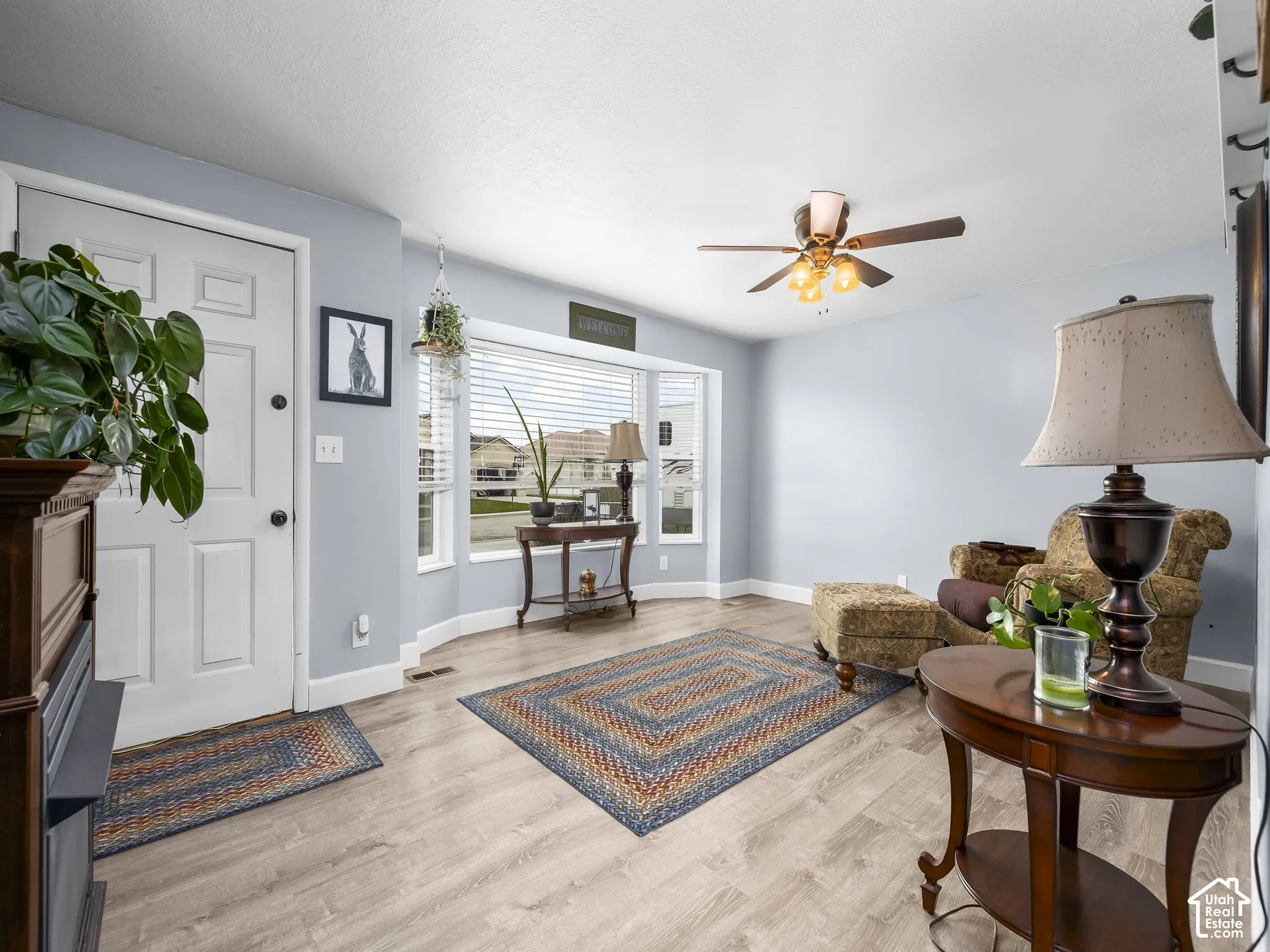 Bright living area featuring wood-finish flooring, a large bay window, and a ceiling fan with integrated lighting