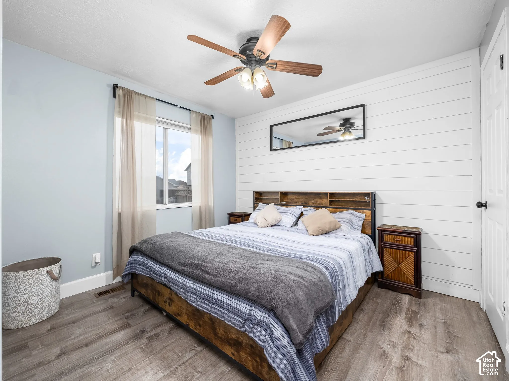 Bedroom featuring wood-finish flooring, horizontal shiplap wall accent, and a central ceiling fan with integrated lighting