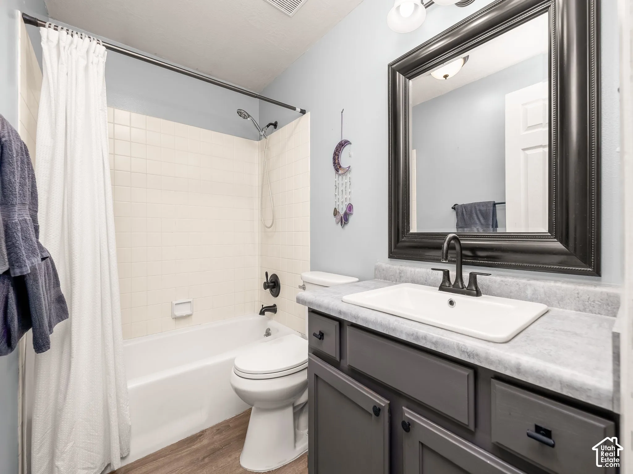 Bathroom featuring a grey vanity with a rectangular drop-in sink, matte black faucet, framed vanity mirror, and wood-finish flooring